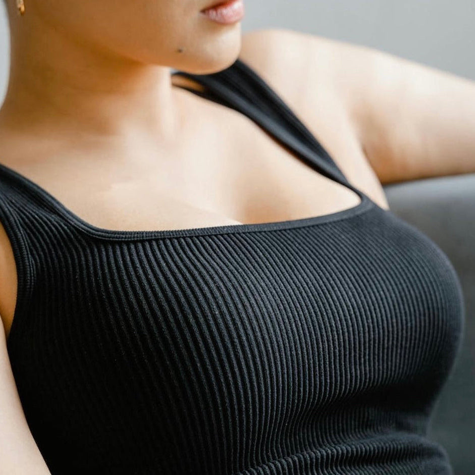 Lady wearing a black ribbed tank top against a neutral background