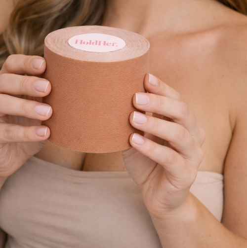 Person holding a roll of boob tape with 'HoldHer' branding.